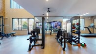 Located at 600 Calvert St in Charlotte, NC, this fitness center is a thoughtfully designed, single-floor facility that combines industrial character with modern amenities. The space is anchored by soaring double-height ceilings and expansive floor-to-ceiling windows that flood the interior with natural light and offer views of the surrounding neighborhood, creating an open and energizing atmosphere.

The layout is divided into distinct workout zones. A dedicated strength training area features a power rack with a weight bench, cable machines, and a dumbbell rack neatly positioned along an exposed brick accent wall. Full-length mirrors are strategically placed throughout, enhancing the sense of space and supporting proper form during workouts. A separate cardio zone houses treadmills and stationary bikes, all positioned to take advantage of the large windows and outdoor views.

A machine training section offers additional strength equipment on warm wood-toned flooring beneath a ceiling fan, while large mirrored walls and integrated display screens add a modern, connected feel. A striking black spiral staircase serves as a bold architectural centerpiece, adding visual interest to the open floor plan.

Near the entrance, a hydration station with a dual water fountain, a bike rack, and a waste station provide convenient, practical amenities. The combination of exposed brick walls, polished concrete-style flooring, and contemporary finishes gives the fitness center a dynamic, welcoming character.