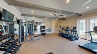 Located at 3215 Midvale Dr in Wilmington, NC, this single-floor fitness center is a comprehensively outfitted facility designed to support a wide range of workout styles and fitness goals. The space features warm neutral walls, light wood-toned flooring, and a ceiling adorned with distinctive decorative wood beams that lend a refined, upscale character. Recessed lighting and multiple ceiling fans ensure the space remains bright and comfortable throughout.

The cardio zone is well-stocked with a row of treadmills, ellipticals, and a stair climber, all positioned near large French doors and windows that invite natural light and offer views to the outdoors. A dedicated strength and functional training area houses a multi-station cable machine, a full rack of dumbbells, a functional training rig complete with TRX suspension straps, kettlebells, and resistance tools, as well as an interactive boxing/reaction training station.

Wall-mounted flat-screen televisions are positioned throughout the space for entertainment during workouts, and full-length mirrors amplify the sense of space while aiding in form and technique. A water fountain is conveniently accessible within the facility. The open, thoughtfully organized layout allows for simultaneous use of multiple equipment zones without congestion, making this fitness center a standout amenity.