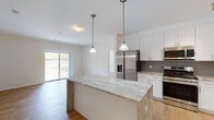Located at 15 Abbey Ln in Danbury, Connecticut, this single-floor residence offers a thoughtfully designed open-concept layout with modern finishes throughout. The kitchen serves as the centerpiece of the home, showcasing floor-to-ceiling white shaker cabinetry, a striking granite waterfall island with pendant lighting overhead, a gray subway tile backsplash, and a full suite of stainless steel appliances including a gas range, built-in microwave, refrigerator with ice maker, and dishwasher. Light hardwood flooring flows seamlessly throughout the entire living space, enhancing the bright and airy atmosphere created by an abundance of natural light. The living area features sliding glass doors that open to a private balcony with outdoor views of the surrounding landscape. The bedrooms are well-proportioned, each with large windows that frame views of the greenery outside and generous closet space. The bathrooms are finished with marble-toned granite vanity tops, white shaker-style cabinetry, matte black hardware and fixtures, tiled tub-shower combinations, and warm neutral floor tiles. Clean white walls and consistent hardwood flooring throughout create a cohesive, contemporary aesthetic across the entire residence.