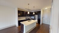 Located along Bluffs Lane in Grapevine, Texas, this single-story unit showcases a contemporary design with a cohesive, open-concept layout. The kitchen serves as a central focal point, featuring rich dark cabinetry that extends floor-to-ceiling, providing generous storage throughout. A large center island with a light quartz countertop and an undermount sink anchors the space, illuminated by stylish pendant lights suspended overhead. Stainless steel appliances, including a French door refrigerator, electric range, and built-in microwave, complement the tile backsplash and track lighting above. The kitchen flows seamlessly into the living area, which is finished with dark hardwood flooring and leads to a set of glass doors opening to an outdoor view, allowing natural light to fill the space. A ceiling fan serves the living area for added comfort. The bedroom offers plush carpeting, a ceiling fan, and a window with exterior views. The bathroom is well-appointed with tile flooring, a tiled shower-tub combination, a dark vanity with countertop, and direct access to a carpeted walk-in closet with built-in shelving, delivering practical, organized storage.