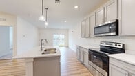 Located in Enola, PA, this single-floor, one-bedroom, one-bathroom residence offers a thoughtfully designed open-concept layout that maximizes every square foot. Light wood-tone luxury vinyl plank flooring flows throughout the main living areas, creating a cohesive and modern aesthetic.

The kitchen is a standout feature, anchored by a large center island with a double stainless steel sink and light quartz countertops. Gray shaker-style cabinetry lines the walls, complemented by stainless steel appliances including a range, microwave, and refrigerator. Globe pendant lights hang above the island, adding a contemporary touch. The kitchen opens directly into the living area, which benefits from a sliding glass door that fills the space with natural light and provides outdoor access.

The bedroom offers a comfortable, carpeted retreat with a window fitted with blinds, allowing for natural light and privacy. A dedicated closet provides convenient storage just off the main entry area.

The bathroom is cleanly finished in white, featuring a gray vanity with an integrated sink, a full soaking tub with a sliding glass shower enclosure, and matching luxury vinyl plank flooring. A hallway connects all areas efficiently, completing this well-organized and move-in-ready home.