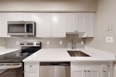 Located at 5270 Duke St in Alexandria, VA, this apartment offers a well-designed single-floor layout with one bedroom, five bathrooms, and thoughtful storage throughout. The open living and dining area is finished with warm hardwood-style flooring and neutral gray walls, creating a bright and clean aesthetic. A sliding glass door leads to a private balcony, allowing natural light to fill the space. The kitchen is outfitted with white shaker-style cabinetry, crisp white quartz countertops, a gray subway tile backsplash, and a full suite of stainless steel appliances including a range, microwave, dishwasher, and refrigerator. The bedroom features plush carpeting, a generous window with blinds for natural light, and a large bifold closet. The bathrooms are finished with light wood-style flooring and include tub-shower combinations with clean white surrounds and chrome fixtures. Five closets throughout the unit provide exceptional storage capacity. A dedicated laundry area adds everyday convenience. The overall design is modern and neutral, offering a move-in-ready environment with consistent, contemporary finishes from room to room.