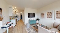 Located in Portland's vibrant SE neighborhood, this single-floor unit at 436 SE 12th Ave offers a well-designed, contemporary living space with a cohesive modern aesthetic. Light-toned luxury vinyl plank flooring runs throughout, unifying the open-concept layout and complementing the crisp white walls.

The living area is bright and inviting, anchored by a large picture window that frames neighborhood greenery and fills the room with natural light. Recessed lighting provides additional illumination throughout the space.

The galley-style kitchen is smartly appointed with high-gloss white cabinetry, open wood-toned shelving, a light quartz countertop, and a grey subway tile backsplash. Stainless steel appliances, including a refrigerator, range, microwave, and dishwasher with brushed gold accents, lend a polished, modern character to the space.

The entryway features a bold dark-painted front door that serves as a stylish design accent, with a nearby closet offering convenient storage. A hallway connects the main living areas to the bathroom and additional spaces, maintaining a logical and functional flow throughout.

The bathroom is clean and well-finished, featuring white cabinetry with an undermount sink, a large mirror, white tile surround, and wood-look flooring consistent with the rest of the unit. The overall ambiance is modern, light, and livable.