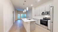 Located at 1350 W Taylor St in Sherman, TX, this well-appointed one-bedroom, one-bathroom unit offers a thoughtfully designed open-concept layout with modern finishes throughout. The kitchen serves as the centerpiece of the living space, anchored by a large center island with a built-in sink and white quartz countertop, illuminated by elegant pendant lighting. Gray cabinetry, a subway tile backsplash, and stainless steel appliances — including a range, microwave, and refrigerator — complete the contemporary kitchen design. Light wood-style flooring extends throughout the main living area, enhancing the bright, airy atmosphere created by recessed lighting and natural light from large windows and a glass-paneled entry door. The bedroom is a comfortable, carpeted retreat featuring a ceiling fan, tall ceilings, and dual windows with blinds that invite natural light. A dedicated closet provides convenient storage. The bathroom is clean and functional, offering a vanity with a white countertop, wood-tone flooring, and a full tub-shower combination with neutral tile surround. The overall design palette of whites, soft grays, and warm wood tones gives the space a cohesive, modern aesthetic well-suited for comfortable everyday living.