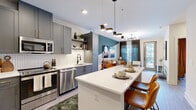 This well-appointed one-bedroom, one-bathroom residence offers a smartly designed open-concept layout that maximizes every square foot. The kitchen is a standout feature, boasting grey shaker-style cabinetry with gold hardware, stainless steel appliances, a herringbone tile backsplash, white quartz countertops, and a central island with seating — ideal for both cooking and casual dining. The kitchen flows seamlessly into the living area, which is anchored by a striking teal accent wall, a sputnik-style ceiling fixture, and large windows with sheer dark drapes that invite abundant natural light. A private balcony extends from the living space, offering outdoor access and exterior views. The bedroom is a comfortable retreat featuring a large window with warm rust-toned curtains, soft blue accent walls, and a dedicated closet. The bathroom is finished with floor-to-ceiling large-format tile, a frameless glass-enclosed walk-in shower with black hardware accents, and an illuminated mirror. Light wood-style flooring runs throughout the main living areas, tying together the contemporary aesthetic of the entire space.
