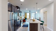 This single-floor residence at 1100 Saint Peters Centre Blvd is designed with a modern aesthetic and functional open layout. The kitchen serves as a central highlight, featuring dark espresso cabinetry extending to the ceiling for ample storage, granite countertops, a white subway tile backsplash, and a full suite of stainless steel appliances. A large kitchen island with seating provides both additional prep space and a natural gathering point. Light wood-style flooring runs throughout the main living areas, complementing the bright, neutral color palette.

The open-concept design allows the kitchen to flow seamlessly into the living area, which receives natural light through large windows dressed with blinds. Ceiling fans are present in multiple rooms for added comfort.

The bedrooms are carpeted and offer a quiet, comfortable retreat, each with windows that bring in natural light. The primary bedroom includes direct access to a full bathroom featuring a granite-topped dark vanity, a tub-shower combination with white tile surround, and wood-look flooring. A second full bathroom mirrors this design. An additional flexible room with carpet offers space suitable for a home office or den. The overall ambiance is clean, contemporary, and move-in ready.