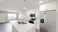 Located at 101 Eastline Rd in Searcy, Arkansas, this well-designed single-floor unit offers a thoughtful layout with modern finishes throughout. The open-concept kitchen and dining area serves as the heart of the home, showcasing crisp white shaker cabinetry, gleaming quartz countertops, a spacious center island with a double undermount sink, and a full suite of stainless steel appliances including a range, over-the-range microwave, and French door refrigerator. Recessed lighting and an adjacent window bring natural light into the space. Wood-look luxury flooring runs throughout the unit, providing a warm, cohesive aesthetic. The living room is generously sized and features a ceiling fan and a large window that invites natural light. The dining area offers direct access to the outdoors through a full-light door flanked by a wide window. Crown molding adds a refined touch in select areas. The spacious primary bedroom includes a ceiling fan, a large window, and direct access to a walk-in closet. The bathroom is well-appointed with white shaker vanity cabinetry, a quartz countertop, an elegant framed mirror, and matte black fixtures. Additional spaces include a laundry area, utility room, hallway, and multiple closets for ample storage.