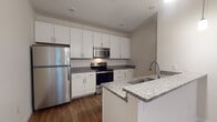 This single-floor unit showcases a clean, contemporary design throughout its thoughtfully arranged layout. The kitchen is a standout feature, offering crisp white shaker-style cabinetry, granite countertops, and a full suite of stainless steel appliances including a refrigerator, range, microwave, and dishwasher. A peninsula with a built-in sink provides additional prep space and casual seating potential, while pendant lighting adds a modern finishing touch. Rich hardwood-style flooring runs throughout the main living and kitchen areas, creating a warm and cohesive aesthetic.

The bathroom continues the refined design language with granite-topped vanity cabinetry, hardwood-style flooring, and a clean, neutral color palette that lends a bright and airy feel. The bedroom is carpeted for comfort and features a large window with blinds that invites natural light and offers views of surrounding greenery, creating a peaceful retreat.

The overall ambiance of the space is modern and well-appointed, with consistent finishes across rooms that contribute to a polished, move-in-ready feel. Neutral walls and carefully selected materials throughout ensure a versatile backdrop suitable for a variety of interior styles.