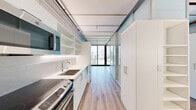Unit 1407 at 3zero3 in Seattle, WA is a thoughtfully designed studio that makes efficient use of its compact footprint without sacrificing style or functionality. The open-plan layout connects the kitchen and living areas seamlessly, creating a sense of continuity throughout the space. Light wood-tone flooring runs underfoot, complementing the crisp white cabinetry and clean-lined finishes that define the interior aesthetic.

The kitchen is well-appointed, featuring stainless steel appliances including a refrigerator, range, microwave, and a stainless undermount sink. White cabinetry and open shelving provide ample storage while keeping the space feeling bright and airy. A glass partition wall with sliding panels adds architectural interest and allows natural light to flow freely between zones.

Floor-to-ceiling sliding glass doors open to a balcony, flooding the interior with natural light and offering panoramic views of the Seattle skyline, neighboring high-rises, and surrounding urban landscape — a striking feature of this elevated unit.

The bathroom is finished with large-format marble-style tiles, a frameless glass walk-in shower with a built-in bench, and sleek chrome fixtures, delivering a spa-like atmosphere. The exposed ceiling track system and industrial-modern detailing add a distinctive urban character throughout the unit.