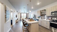 This well-designed one-bedroom, one-bathroom unit in Broomfield, Colorado offers a thoughtful layout across a single floor. The open-concept kitchen and living area serves as the heart of the home, featuring light wood-tone cabinetry, quartz countertops, a full stainless steel appliance suite, a tiled backsplash, and a central island with bar seating illuminated by pendant lighting. The kitchen flows seamlessly into a bright, spacious living room with hardwood-style flooring, a ceiling fan, and large windows that invite abundant natural light and outdoor views. A private balcony extends the living space outdoors. The generously sized bedroom is carpeted for comfort, fitted with a ceiling fan, and receives excellent natural light through large windows with outdoor views. It is served by two closets, including a walk-in closet with built-in shelving for ample storage. The full bathroom features a soaking tub and shower combo with decorative tile accents, a floating wood-tone vanity with a quartz countertop, and hardwood-style flooring. Additional conveniences include an in-unit laundry area. The unit's modern, neutral palette and contemporary finishes create a clean, cohesive aesthetic throughout.
