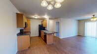 Located at 2861 S Nettleton Ave in Springfield, Missouri, this single-story home offers a well-organized layout with four bedrooms, two full bathrooms, and a practical mix of living spaces. The open-concept kitchen and dining area is a central highlight, featuring warm wood-toned cabinetry, dark granite-style countertops, a kitchen island with seating, and black appliances including a range, microwave, refrigerator, and dishwasher. Wood-style flooring runs throughout the main living areas and kitchen, lending a cohesive and easy-to-maintain aesthetic. The spacious living room is bathed in natural light from a large sliding glass door fitted with vertical blinds and includes a ceiling fan overhead. Two hallways connect the living spaces to the bedrooms, offering an efficient flow throughout the home. The bedrooms are carpeted and equipped with ceiling fans, with the generously sized primary bedroom providing ample space. Six closets are distributed throughout, ensuring abundant storage. The bathrooms feature wood-look tile flooring, white vanities, and full tub-shower combinations. A dedicated laundry room and utility room add further convenience. The clean, neutral palette throughout creates a bright, move-in-ready atmosphere.