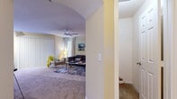 This single-floor residence offers a thoughtfully designed layout that balances comfort and functionality across its living spaces. The living room serves as the heart of the home, featuring plush wall-to-wall carpeting, a ceiling fan, and a built-in arched display niche with open shelving — an ideal spot for a television and decorative accents. Natural light filters in through large windows dressed with sheer curtains, creating a warm and inviting atmosphere. An entry foyer with tile flooring leads seamlessly into the main living area via an arched passageway, adding a charming architectural touch.

The kitchen is efficiently arranged in a galley-style layout, outfitted with rich wood cabinetry, dark granite-style countertops, and black appliances including a full-size refrigerator and range. A peninsula with bar seating bridges the kitchen to the living space, making it ideal for casual dining and entertaining. A dedicated laundry area is conveniently accessible nearby.

The bedroom is a restful retreat, highlighted by a soothing accent wall, ceiling fan, plush carpeting, and a generously sized walk-in closet. The bathroom features a dual-sink vanity with wood cabinetry, white countertops, and tile flooring, with an arched opening connecting it gracefully to the rest of the home.