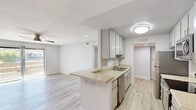 Located at 2925 Escoba Drive in Palm Springs, CA, this well-appointed one-bedroom, one-bathroom residence offers a clean, modern aesthetic throughout its single-floor layout. Light wood-tone flooring flows seamlessly across every room, creating a cohesive and airy feel. The open-concept living, dining, and kitchen area forms the heart of the home, anchored by a functional peninsula with granite-style countertops that doubles as a breakfast bar. The kitchen is fully equipped with stainless steel appliances — including a range, microwave, and dishwasher — complemented by gray shaker-style cabinetry and a double basin sink. Ceiling fans with integrated lighting are found in both the living area and bedroom, supporting comfort in the warm Palm Springs climate. The spacious bedroom offers recessed lighting, a generous built-in open closet with shelving, and a sliding glass door that connects directly to a private balcony, allowing for natural light and outdoor access. The full bathroom features a tub-shower combination with a clean white finish. A hallway connects the main living areas to the bedroom and bathroom, completing this efficiently designed and thoughtfully updated residence.