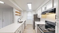 Located in Portland, OR along SW Beaverton Hillsdale Hwy, this single-floor, 3-bedroom, 2-bathroom home offers a well-designed layout with a clean, contemporary aesthetic. The galley-style kitchen is a standout feature, showcasing white shaker cabinets with matte black hardware, white quartz countertops, a subway tile backsplash, a stainless steel sink with a black faucet, open wood floating shelves, and stainless steel appliances including a refrigerator and range. A skylight overhead fills the space with natural light. The kitchen flows directly into the open living area, which features light wood-style flooring and a ceiling fan. The three bedrooms offer comfortable layouts; the primary bedroom is bathed in natural light and features the same wood flooring, while the additional bedrooms are carpeted with neutral tones and access to the hallway. Both bathrooms are clean and functional, each with a tub-shower combination, white vanity with quartz countertop, and light flooring. A dedicated laundry area includes an in-unit washer, overhead cabinetry, and a window with natural light. The consistent white palette and updated finishes throughout give the home a fresh, move-in-ready feel.