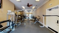 This fitness center in Elgin, South Carolina offers a well-appointed, single-level exercise facility designed to support a full range of workout routines. The space is divided into distinct functional zones, beginning with a dedicated cardio area housing multiple Matrix treadmills positioned in front of a full-length wall mirror, which visually expands the room and allows users to monitor their form. Recessed panel lighting and ceiling fans are installed throughout, maintaining a comfortable and well-lit environment during workouts.

The strength training area is generously equipped with a variety of resistance machines, cable systems, a multi-use weight bench, and a well-stocked dumbbell rack spanning a wide range of weights. Free weights, medicine balls, stability balls, and a flat utility bench round out the available equipment. Large windows along one wall allow natural light to filter in and provide views of an outdoor pool area, adding a bright, open feel to the space.

Crown molding along the ceiling line and neutral warm-toned walls contribute a polished aesthetic that distinguishes this facility from a purely utilitarian gym. A wall-mounted television is also present, offering entertainment during longer training sessions. The durable flooring throughout accommodates both heavy equipment and functional movement exercises effectively.