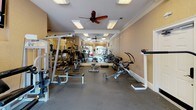 This fitness center in Elgin, South Carolina offers a well-appointed, single-level exercise facility designed to support a full range of workout routines. The space is divided into distinct functional zones, beginning with a dedicated cardio area housing multiple Matrix treadmills positioned in front of a full-length wall mirror, which visually expands the room and allows users to monitor their form. Recessed panel lighting and ceiling fans are installed throughout, maintaining a comfortable and well-lit environment during workouts.

The strength training area is generously equipped with a variety of resistance machines, cable systems, a multi-use weight bench, and a well-stocked dumbbell rack spanning a wide range of weights. Free weights, medicine balls, stability balls, and a flat utility bench round out the available equipment. Large windows along one wall allow natural light to filter in and provide views of an outdoor pool area, adding a bright, open feel to the space.

Crown molding along the ceiling line and neutral warm-toned walls contribute a polished aesthetic that distinguishes this facility from a purely utilitarian gym. A wall-mounted television is also present, offering entertainment during longer training sessions. The durable flooring throughout accommodates both heavy equipment and functional movement exercises effectively.