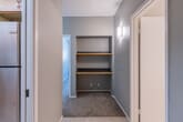 This single-floor unit offers a practical and well-organized layout across several distinct living areas. The galley-style kitchen is efficiently designed with warm honey-toned wood cabinetry lining both walls, granite-look countertops, a stainless steel refrigerator, a white electric range, and a double sink. A skylight-style ceiling fixture provides bright overhead lighting, while tile flooring adds durability throughout the kitchen and connecting hallway.

The hallway connects the kitchen to the rest of the unit and features a built-in shelving nook with two wood-toned shelves, a wall-mounted light fixture, and carpeted flooring — offering a functional space for storage or a small home office setup.

The spacious living area is carpeted and finished with neutral gray walls and a textured ceiling. A baseboard heating unit runs along the wall, and a sliding glass door opens to an outdoor balcony, allowing natural light to fill the room. An adjacent dining or secondary living space shares a similar neutral palette with carpet flooring and a ceiling-mounted light fixture.

The bedroom is generously sized with plush carpet, a wide window fitted with vertical blinds, a baseboard heater, and a textured ceiling. The bathroom includes a full-size tub and shower combo with white tile surround, chrome grab bars and fixtures, and a clean, functional design throughout.