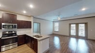 This single-story, two-bedroom, two-bathroom residence offers a thoughtfully designed open-concept layout that seamlessly connects the kitchen, dining, and living areas. The kitchen serves as a central focal point, featuring rich dark espresso cabinetry extending to the ceiling, stainless steel appliances including a French door refrigerator, electric range, and microwave, complemented by granite countertops and a double-basin sink set within a peninsula that provides additional seating and prep space. A white subway tile backsplash adds a clean, contemporary touch.

The living area is generously sized with warm hardwood-style flooring, recessed lighting, a ceiling fan, and access to an outdoor space through a glass door, allowing for natural light. Both bedrooms are carpeted and include ceiling fans and ample natural light from windows with blinds. Each bedroom features a walk-in or standard closet.

The two bathrooms offer distinct configurations: one includes a tub-shower combo with white tile surround, while the other features a glass-enclosed walk-in shower with tile walls. Both bathrooms are finished with clean, neutral tones and wood-style flooring.