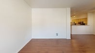 This single-floor residence offers a thoughtfully designed layout with a clear separation between living and sleeping areas. The main living space features warm hardwood-style flooring that extends through an open hallway, creating a cohesive and inviting atmosphere. A partial wall column adds architectural definition between the living area and the corridor leading to the bedrooms.

The kitchen is well-equipped with stainless steel appliances, including a range, over-the-range microwave, refrigerator, and dishwasher. Light wood cabinetry pairs with granite-style countertops to provide ample storage and workspace, all set on hardwood-style flooring.

The bedrooms are finished with plush carpeting and feature baseboard heating units beneath windows fitted with blinds, allowing natural light to filter in. One bedroom includes a ceiling fan and access to an en-suite bathroom and a dedicated closet area. The bathrooms feature arched ceilings, hardwood-style flooring, and clean white fixtures. The full bathroom includes a vanity with granite-style countertops, a tub-shower combination, and a large mirror. A second, more compact bathroom offers a toilet and towel bar. Overall, the space presents a clean, neutral palette throughout.
