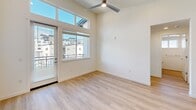 This well-designed single-floor residence offers three bedrooms, two bathrooms, a dedicated laundry room, and an open-concept kitchen and living area. Light hardwood-style flooring flows consistently throughout the home, contributing to a clean and cohesive aesthetic.

The kitchen is a standout feature, outfitted with dark charcoal cabinetry, crisp white countertops, and a full suite of stainless steel appliances including a refrigerator, range, microwave, and dishwasher. A peninsula with an undermount sink and pendant lighting above serves as both a functional workspace and a natural divider between the kitchen and living area. The living room benefits from tall ceilings, a ceiling fan, and floor-to-ceiling windows with transom panels above, allowing abundant natural light and providing access to an outdoor balcony.

The three bedrooms are bright and well-proportioned, each featuring windows with exterior views. The primary bedroom is notably spacious, with elevated ceilings, large windows, and balcony access. The two bathrooms are finished with dark vanities and white countertops, maintaining the modern design language found throughout the home. A dedicated laundry room houses a full-size top-loading washer and dryer with overhead shelving for added storage convenience.