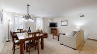 This single-floor residence offers a practical and comfortable layout across two bedrooms and one bathroom. The open living and dining area serves as the heart of the home, featuring plush carpeting, neutral white walls, and windows that invite natural light. The living area provides ample space for relaxing, while the adjoining dining space is defined by a pendant chandelier overhead, making it an ideal spot for meals and gatherings.

The kitchen is equipped with warm honey-toned wood cabinetry, granite-patterned countertops, and tile flooring. It offers generous storage and counter space, complete with a double sink and full appliance suite including a range and over-the-range microwave.

The primary bedroom is a spacious retreat featuring soft carpeting, a large closet with classic wood sliding doors, and enough room to comfortably accommodate a king-sized bed and additional furnishings. The second bedroom offers a similar cozy aesthetic.

The bathroom is finished with tile flooring, a modern wood-toned vanity with a white countertop, a framed mirror, and a shower-tub combination accented by a decorative curtain.

Throughout the home, clean white walls, consistent flooring transitions, and neutral tones create a cohesive and inviting atmosphere.