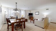 This single-floor residence offers a practical and comfortable layout across two bedrooms and one bathroom. The open living and dining area serves as the heart of the home, featuring plush carpeting, neutral white walls, and windows that invite natural light. The living area provides ample space for relaxing, while the adjoining dining space is defined by a pendant chandelier overhead, making it an ideal spot for meals and gatherings.

The kitchen is equipped with warm honey-toned wood cabinetry, granite-patterned countertops, and tile flooring. It offers generous storage and counter space, complete with a double sink and full appliance suite including a range and over-the-range microwave.

The primary bedroom is a spacious retreat featuring soft carpeting, a large closet with classic wood sliding doors, and enough room to comfortably accommodate a king-sized bed and additional furnishings. The second bedroom offers a similar cozy aesthetic.

The bathroom is finished with tile flooring, a modern wood-toned vanity with a white countertop, a framed mirror, and a shower-tub combination accented by a decorative curtain.

Throughout the home, clean white walls, consistent flooring transitions, and neutral tones create a cohesive and inviting atmosphere.