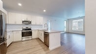 This well-appointed single-floor residence offers a clean, modern aesthetic highlighted by light wood-look flooring and a bright, neutral color palette that runs throughout the space. The open-concept kitchen serves as the heart of the unit, showcasing white flat-panel cabinetry, a classic white subway tile backsplash, quartz countertops, and a full suite of stainless steel appliances including a range, microwave, refrigerator, and dishwasher. A peninsula with an extended counter provides additional workspace and casual seating, flowing seamlessly into the open living area beyond. Large windows fitted with horizontal blinds fill the living space with natural light and offer views of the surrounding neighborhood. The bedrooms are generously proportioned, each featuring the same light wood-look flooring, neutral walls, and well-sized windows that invite ample daylight. One bedroom benefits from a spacious walk-in closet equipped with wire shelving for organized storage. The bathroom features a clean, contemporary design with white cabinetry, a quartz-topped vanity with an undermount sink, and a large mirror. The overall ambiance of the space is fresh, bright, and move-in ready, presenting a cohesive modern design throughout.