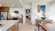 Located on Walnut Street in Philadelphia's desirable Rittenhouse Square neighborhood, this thoughtfully designed single-floor residence offers a seamless blend of modern architecture and refined interior design. The entry foyer makes an immediate impression with a striking abstract wall mural, setting a stylish tone that carries throughout the space. Light wood-style flooring flows continuously across all rooms, complemented by crisp white walls and recessed lighting.

The open-concept living and dining area is defined by expansive floor-to-ceiling windows on multiple sides, flooding the space with natural light and framing sweeping views of the Philadelphia skyline and surrounding urban landscape. A contemporary chandelier anchors the living room, while the dining area features a sleek marble-top table adjacent to a glass-panel balcony door.

The kitchen is outfitted with two-tone cabinetry — white upper cabinets paired with warm wood lower cabinets — along with stainless steel appliances and a clean quartz countertop. The primary bedroom showcases a dramatic upholstered accent wall with decorative mirrors, large windows, and direct access to a well-appointed en-suite bathroom. The bathroom includes a wood-toned vanity and connects to a spacious walk-in closet with built-in shelving. A clean, light-filled hallway with louvered closet doors connects the private areas of the residence efficiently.
