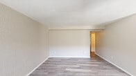 This single-floor unit offers a straightforward, functional layout designed for comfortable everyday living. The main living area is generously proportioned, featuring light grey wood-look laminate flooring, neutral beige walls with a subtle texture, and a textured ceiling throughout. A structural beam detail runs across the upper wall, adding architectural definition to the space. Multiple electrical outlets are positioned conveniently along the walls, and an open passage leads to the rest of the unit.

The kitchen is efficiently arranged in a galley-style configuration, equipped with white cabinetry, a light granite-patterned countertop, a double-basin sink, and black appliances including a refrigerator, gas range, and dishwasher. A flush-mount ceiling fixture provides direct overhead lighting, and the same laminate flooring extends throughout.

The bedroom features plush carpeted flooring, a window that allows natural light to enter, and a textured ceiling. A walk-in closet with a built-in rod provides practical storage, while an additional standard closet with bifold doors offers further organization options.

The bathroom includes a full-size soaking tub fitted with a clean white paneled surround. Overall, the unit presents a neutral, move-in-ready palette throughout.