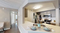 This single-floor residence offers a thoughtfully designed layout that balances comfort and functionality throughout. The kitchen serves as a central highlight, featuring gray cabinetry with a built-in wine rack, stainless steel appliances including a refrigerator, electric range, and over-the-range microwave, and light quartz countertops that extend to a convenient peninsula with a stainless steel sink. Wood-look flooring runs through the kitchen, and a dedicated in-unit laundry closet is conveniently accessible nearby. The open sightline from the kitchen connects seamlessly to the hallway and living areas, enhancing the sense of flow throughout the home. Multiple bedrooms are finished with plush wall-to-wall carpeting, neutral wall tones, and ceiling fans with light fixtures, creating a comfortable and relaxed atmosphere. Natural light enters through blinded windows in each bedroom. Walk-in closet access is present in at least one bedroom, offering generous storage. The bathrooms are finished with matching gray vanity cabinetry, white quartz countertops, large mirrors, and wood-look flooring. One bathroom features a shower-tub combination, while a second provides a single-sink vanity with walk-in closet access. Textured ceilings are consistent throughout, contributing to the space's cohesive residential character.