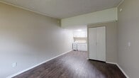 Located at 300 Jones Mill Rd in Statesboro, Georgia, this single-floor unit offers a straightforward and functional layout designed for efficient everyday living. The main living area is open and airy, finished with rich, dark hardwood-style flooring that runs throughout the space, providing a clean and cohesive look. Neutral-toned walls keep the interior bright and versatile, complementing the textured ceiling overhead.

Natural light enters through a large window fitted with horizontal blinds, offering views of surrounding greenery and lending the space a welcoming atmosphere. A wall-mounted PTAC unit provides both heating and cooling directly within the living area. The front entry door is solid and well-positioned alongside the window, creating a practical and uncluttered entryway.

The kitchen is neatly tucked at the rear of the open floor plan and features white cabinetry, a countertop with a single-basin sink, and a white range with an electric cooktop — providing all essential cooking amenities in a compact, organized footprint. A tall built-in storage closet positioned between the living and kitchen areas offers convenient additional storage.

Overall, this unit presents a clean, no-frills living environment that is well-suited for those seeking a practical and low-maintenance space in Statesboro.