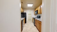 This single-floor residence offers a practical and comfortable layout across several well-defined spaces. The galley-style kitchen is a functional highlight, lined on both sides with warm honey-toned wood cabinetry and light granite-look countertops. It is fully equipped with black appliances, including a refrigerator, electric range, built-in microwave, and dishwasher. A skylight-style overhead fixture keeps the kitchen bright and welcoming. The kitchen leads to a dedicated laundry room housing a full-size Whirlpool washer and dryer, adding significant everyday convenience. The living areas are finished with plush wall-to-wall carpeting in a neutral beige tone, creating a warm and inviting atmosphere. A sliding glass door in the main living space fills the room with natural light and provides access to an outdoor area with views of surrounding greenery. The space includes two full bathrooms, each finished with matching tile flooring and warm wood vanity cabinetry. One bathroom features a shower-tub combination with a framed sliding glass enclosure, while the second offers a similar tub-shower setup alongside a granite-top vanity. Throughout the residence, a consistent neutral color palette and clean finishes contribute to a cohesive and move-in-ready aesthetic.