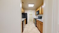 This single-floor residence offers a practical and comfortable layout across several well-defined spaces. The galley-style kitchen is a functional highlight, lined on both sides with warm honey-toned wood cabinetry and light granite-look countertops. It is fully equipped with black appliances, including a refrigerator, electric range, built-in microwave, and dishwasher. A skylight-style overhead fixture keeps the kitchen bright and welcoming. The kitchen leads to a dedicated laundry room housing a full-size Whirlpool washer and dryer, adding significant everyday convenience. The living areas are finished with plush wall-to-wall carpeting in a neutral beige tone, creating a warm and inviting atmosphere. A sliding glass door in the main living space fills the room with natural light and provides access to an outdoor area with views of surrounding greenery. The space includes two full bathrooms, each finished with matching tile flooring and warm wood vanity cabinetry. One bathroom features a shower-tub combination with a framed sliding glass enclosure, while the second offers a similar tub-shower setup alongside a granite-top vanity. Throughout the residence, a consistent neutral color palette and clean finishes contribute to a cohesive and move-in-ready aesthetic.
