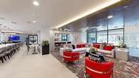 Located at 15915 Kingfield Dr in Houston, TX, this single-story community amenity space delivers a bold, contemporary design across a generously proportioned open floor plan. The interior is immediately striking, anchored by a cohesive red, white, and gray color palette carried throughout the furnishings, patterned carpeting, and accent décor.

The main lounge area features plush gray sectional sofas and vibrant red accent chairs arranged around a sleek black coffee table, all set atop an abstract, multi-toned area rug. A large wall-mounted display screen serves as a focal point, while cove lighting and a reflective metallic ceiling treatment add a sophisticated, upscale ambiance. Floor-to-ceiling glass panels allow abundant natural light and views to the surrounding exterior.

Adjacent to the lounge, a fully equipped kitchen showcases a marble-topped island with seating, stainless steel appliances, and pendant lighting, making it ideal for community gatherings and events. A circular dining area with a statement ceiling medallion and sculptural centerpiece connects this space to the rest of the room.

A dedicated game room includes a billiards table, a high-top bar station with modern seating, and sheer-draped windows that soften the light. The entry vestibule features additional seating vignettes with wall-mounted TVs, offering a welcoming transition into the space. Large-format porcelain tile flooring in the open areas provides a clean contrast to the richly patterned carpet zones throughout.