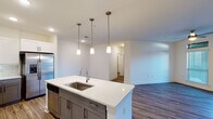 This single-floor residence showcases a contemporary open-concept design that seamlessly connects the kitchen and living areas. The kitchen serves as the centerpiece, anchored by a large island with a undermount sink, quartz countertops, and three pendant lights overhead. Cabinetry features a two-tone design with white upper cabinets and gray lower cabinets, complemented by a classic subway tile backsplash. Stainless steel appliances, including a refrigerator with ice maker, range, and microwave, complete the kitchen. Wood-look plank flooring extends throughout the main living areas, adding warmth and cohesion. The spacious living area benefits from ceiling fans and recessed lighting, with French doors providing access to the outdoors.

The bedrooms are carpeted for comfort, with the primary suite offering a walk-in closet and en-suite bathroom access. Both bathrooms are well-appointed with gray shaker-style vanities, quartz countertops, undermount sinks, large mirrors, and tub-shower combinations. The overall aesthetic throughout is clean and modern, with crisp white walls, consistent finishes, and thoughtful details creating a polished, move-in-ready environment.