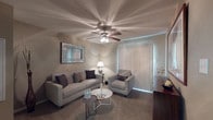 This single-floor residence offers a thoughtfully designed layout that balances comfort and functionality across its key living spaces. The living room serves as the centerpiece of the home, featuring a ceiling fan with integrated lighting, soft carpeted flooring, and a decorative framed mirror as a focal point on the neutral-toned walls. A sliding glass door dressed with vertical blinds allows natural light to fill the space, creating a warm and inviting atmosphere. Seating is arranged around a sleek round coffee table, lending the room a modern yet relaxed character.

The kitchen is outfitted with rich dark wood cabinetry, granite-style countertops, and a full suite of black appliances including a refrigerator, range, microwave, and dishwasher, all set atop durable hardwood-style flooring. Adjacent to the kitchen, the dining area accommodates an intimate glass-top table with upholstered chairs beneath framed wall art, ideal for casual meals.

The bedrooms are carpeted and serene, each featuring ceiling fans and natural light from window blinds. The primary bedroom includes direct access to a walk-in closet. The bathroom presents a generous vanity with dark wood cabinetry and granite-style countertops, complemented by a large mirror for an open, functional feel.