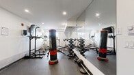 Located at 728 Meaford Ave in Langford, BC, this fitness room offers a compact yet efficiently utilized space designed to support a well-rounded workout routine. The room features durable rubber flooring throughout, crisp white walls, and recessed pot lighting that keeps the environment bright and functional.

The space is thoughtfully equipped with a varied selection of cardio machines, including a treadmill, stationary spin bikes, and an elliptical trainer, providing ample options for cardiovascular exercise. A large wall-mounted mirror spans one side of the room, enhancing the sense of space and allowing users to monitor their form during workouts.

For strength training, the room includes a multi-function cable machine, a weight bench with barbells, a pull-up and dip station, and freestanding Century heavy punching bags — catering to both resistance and combat-style training. Additional accessories such as step platforms and a motivational fitness poster round out the amenities.

A wall-mounted flat-screen TV adds a touch of convenience for entertainment during workouts. Natural light filters in through a window on one wall, contributing to a welcoming atmosphere. The room's practical layout maximizes every corner, making it a well-appointed fitness facility for residents at this Langford address.