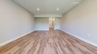 This newly constructed three-floor home offers a well-designed layout across five bedrooms, three bathrooms, and multiple living areas. The main floor is the largest level, featuring an open-concept kitchen equipped with slate-blue shaker cabinetry, a stainless steel farmhouse sink, subway tile backsplash, pendant lighting, and stainless steel appliances, including a dishwasher. The kitchen flows seamlessly into the living and dining areas, where warm hardwood floors extend throughout. Sliding glass doors lead to a freshly built wooden deck, offering pleasant outdoor views. The bathrooms are finished with a clean, modern aesthetic, featuring grey vanities, black hardware accents, and a mix of wood-look and tile flooring. The upper floor houses the bedrooms, each carpeted for comfort and equipped with ceiling fans. Bedrooms include built-in closets, and the primary bedroom provides a generous, well-proportioned retreat. The lower floor offers additional living space with hardwood-style flooring, a wall-mounted mini-split unit, and sliding doors that bring in natural light. Two staircases connect the floors, enhancing circulation throughout the home. The neutral grey palette and clean white trim present a fresh, move-in ready atmosphere.