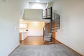 This thoughtfully designed single-floor space offers a distinctive layout highlighted by a dramatic two-story ceiling in the main living area, creating an immediate sense of openness and volume upon entry. A standout architectural feature is the sleek black spiral staircase, which rises to an upper loft area enclosed by a metal railing, adding visual interest and vertical dimension to the space.

The open-concept kitchen is equipped with ample white cabinetry accented by warm wood trim, generous counter space along a peninsula that separates the kitchen from the adjacent dining area, a stainless steel sink, electric range, dishwasher, and refrigerator. A chandelier fixture provides warm overhead lighting to the dining space.

The living area transitions into carpeted rooms, offering comfortable and quiet spaces suited for rest or flexible use. One room features a sliding glass door with vertical blinds, filling the space with natural light and providing direct access to an outdoor balcony with views of surrounding greenery.

Two full bathrooms each include a tub-shower combination, toilet, single-sink vanity with white cabinetry, and a large mirror. Wood-look flooring runs through the kitchen, dining, and bathroom areas, while neutral-toned carpet covers the remaining rooms, contributing to a cohesive and practical overall aesthetic.