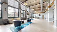 Located at 57 Charter Oak Ave in Hartford, CT, this single-floor communal amenity space blends industrial heritage with modern design. Soaring ceilings with exposed ductwork and original wood beams define the open main hall, where floor-to-ceiling grid-pane windows flood the interior with abundant natural light and offer views of the surrounding neighborhood.

The main lounge area features tufted leather sofas, accent chairs, and vibrant blue area rugs, creating an inviting gathering space anchored by a wall-mounted television and decorative cabinetry. Pendant lighting throughout adds warmth and character to the high-ceilinged rooms.

The fully equipped kitchen area includes stainless steel appliances, granite countertops with a breakfast bar, wood-toned cabinetry, and pendant lighting — ideal for entertaining or casual use. Adjacent dining and high-top seating areas provide additional flexible space for socializing.

A dedicated game room rounds out the amenities, showcasing a full-size billiards table beneath statement pendant fixtures, flanked by tall industrial windows that continue the building's distinctive architectural character. A ping-pong table adds to the recreational offerings.

Throughout the space, polished concrete flooring, exposed structural columns, and carefully curated furnishings strike a balance between the building's industrial past and a contemporary, welcoming atmosphere.