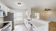 This single-story, 3-bedroom, 2-bathroom home offers a clean, modern interior designed for comfortable everyday living. The open-concept kitchen and living area serves as the heart of the home, featuring crisp white cabinetry with matte black hardware, light quartz countertops, stainless steel appliances including a refrigerator, range, microwave, and dishwasher, and a peninsula that opens toward the living space. Natural light pours in through multiple windows fitted with blinds throughout the home. The living room is bright and airy, with light wood-style vinyl plank flooring, a ceiling fan, and direct access to the front entry. A central hallway connects the three bedrooms, each of which continues the light flooring and features ceiling fans, ample natural light from exterior-facing windows, and closet space. The generously sized primary bedroom includes a walk-in closet. The two bathrooms maintain a consistent, clean aesthetic with white vanities, matte black fixtures, and matching flooring. Textured ceilings are present throughout, adding subtle architectural character. The overall ambiance is bright, neutral, and move-in ready, reflecting a cohesive and functional design sensibility.