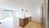 This 1-bedroom, 1-bathroom residence in Farmington, MN offers a thoughtfully designed single-floor layout with modern finishes throughout. The open-concept kitchen and living area serves as the heart of the home, featuring light hardwood-style flooring, crisp white walls, and abundant natural light. The kitchen is appointed with rich walnut-toned cabinetry accented by gold hardware, a white quartz waterfall island with an undermount sink and matte black faucet, stainless steel appliances including a refrigerator, range, microwave, and dishwasher, and a white tile backsplash. Striking black pendant lights with gold interiors illuminate the space. The living area opens via a sliding glass door to a private balcony with exterior views. The bedroom is a bright, tranquil space with a large window allowing ample natural light. A walk-in closet provides generous storage. The bathroom features a dual-sink vanity with walnut cabinetry and quartz countertops, matte black fixtures, a soaking tub with shower, and a large mirror. Additional spaces include a utility room and ample in-unit storage, completing this well-appointed modern residence.