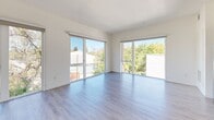 Located at 1517 H Street in downtown Sacramento, this apartment offers a well-designed layout across a single floor, accommodating three bedrooms and two full bathrooms. The open-concept living and kitchen area serves as the heart of the unit, featuring light wood-tone flooring, clean white walls, and large sliding glass doors and floor-to-ceiling windows that flood the space with natural light while framing views of the surrounding treetops and Sacramento skyline.

The kitchen is outfitted with two-tone cabinetry—combining warm wood lower cabinets with sleek gray uppers—stainless steel appliances including a range, microwave, and dishwasher, and a white subway tile backsplash. A hallway connects the living areas to the bedrooms, each carpeted in neutral tones with closets and generous window exposure. The primary bedroom features large sliding glass doors with outdoor views.

Both bathrooms continue the modern aesthetic with warm wood vanities, white countertops, large mirrors, and marble-style tiled shower surrounds. One bathroom includes a tub-shower combination, while the other features an accessible layout with grab bars and a walk-in shower. The overall design is clean, contemporary, and bright throughout.