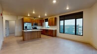 Located on the fifth floor at 1102 West Summit Parkway in Spokane, Washington, this single-level residence combines modern design with functional living spaces. The heart of the home is a generously sized kitchen featuring rich warm-toned wood cabinetry, crisp white countertops, a central island, and a full suite of stainless steel appliances including a refrigerator with ice maker, range, microwave, and dishwasher. Large black-framed windows flood the kitchen and adjoining living area with natural light while offering sweeping views of the Spokane cityscape. The open living area extends to a private balcony accessible through a glass-paneled door, further embracing the urban panorama. Bedrooms are carpeted for comfort and include generous closet space, with windows that continue the theme of natural light and outdoor views. Two bathrooms are finished with wood vanities, white countertops, and tub-shower combinations with chrome fixtures. A dedicated laundry room houses a full-size front-loading washer and dryer alongside overhead cabinetry for additional storage. Recessed lighting throughout, neutral wall tones, and consistent design details give the entire residence a clean, contemporary feel well-suited for modern urban living.