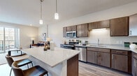 Located at 215 3rd St in Wausau, WI, this thoughtfully designed one-bedroom, one-bathroom unit offers a comfortable and efficient layout across a single floor. The open-concept kitchen and living area serves as the heart of the space, featuring rich dark-toned cabinetry, stainless steel appliances including a refrigerator, range, microwave, and dishwasher, and a light quartz countertop island with bar seating — ideal for both cooking and casual dining. Wood-look plank flooring runs throughout the main living areas, adding warmth and continuity. The living room is bright and inviting, with recessed lighting and a sliding glass door that opens to a private balcony with views of the surrounding streetscape. The bedroom offers a cozy, carpeted retreat with multiple windows that bring in natural light and include a closet for ample storage. The bathroom is finished with dark wood cabinetry, a single vanity with stone countertop, wood-look tile flooring, and a walk-in shower. A dedicated laundry area houses a stacked full-size washer and dryer unit alongside additional shelving. The hallway connects all rooms efficiently, completing a well-organized and modern floor plan suited for everyday living.