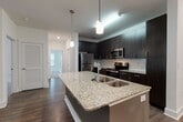This well-appointed single-floor residence offers a thoughtfully designed layout that balances modern finishes with functional living spaces. The kitchen serves as the centerpiece of the home, showcasing a large granite-topped island with an undermount sink, elegant pendant lighting, and dark espresso cabinetry that extends to the ceiling. Stainless steel appliances — including a refrigerator, range, and built-in microwave — complement the white subway tile backsplash, creating a refined, contemporary aesthetic. Wood-look flooring flows throughout the main living and kitchen areas, adding warmth and continuity.

The bathrooms feature matching granite countertops with undermount sinks, dark wood cabinetry, large mirrors, and wood-look flooring. One bathroom includes a glass-enclosed walk-in shower with white tile surround, maintaining the home's clean, modern style.

The bedrooms are carpeted and generously sized, each offering natural light through multiple windows with blinds. Ceiling fans provide comfortable climate control, and closets offer practical storage solutions.

A dedicated laundry room with a full-size washer and dryer is conveniently accessible from the main living area, adding to the home's everyday functionality. Overall, the space presents a cohesive, move-in-ready environment with quality finishes throughout.