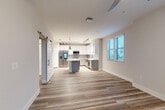 Located in Melbourne, FL, this thoughtfully designed one-bedroom, two-bathroom residence offers a clean, modern aesthetic throughout its single-floor layout. The open-concept kitchen and living area serves as the heart of the home, featuring light wood-look flooring, a central island with a quartz countertop, white upper cabinetry paired with gray lower cabinets, stainless steel appliances, and industrial-style pendant lighting complemented by track lighting. Multiple windows with blinds invite abundant natural light, creating a bright and airy atmosphere. A charming barn door adds a stylish architectural detail to the living space. The bedroom is carpeted for comfort and includes a well-organized walk-in closet outfitted with built-in shelving, hanging rods, and ample storage. The bathrooms are finished to a high standard, featuring sage-toned cabinetry, quartz countertops, vessel sinks, brushed nickel hardware, and a glass-enclosed walk-in shower with tile surround. A dedicated laundry area includes built-in cabinetry with quartz countertops for added convenience. Neutral wall tones and consistent wood-look flooring throughout the main areas tie the space together in a cohesive, contemporary style.