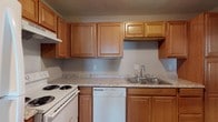 Located at 3605 Gautier Vancleave Rd in Gautier, Mississippi, this single-floor unit offers a practical and comfortable layout designed for everyday living. The kitchen is a functional highlight, featuring warm honey-toned wood cabinetry with ample upper and lower storage, light granite-style countertops, and wood-look flooring. It is fully equipped with a white electric range, dishwasher, refrigerator, and a stainless steel sink — all thoughtfully arranged for efficient use of the space. A pass-through window connects the kitchen to the living area, enhancing the open feel between rooms. The living area is generously proportioned, finished with plush wall-to-wall carpeting and neutral-toned walls that create a clean, versatile backdrop. The bedrooms continue the carpeted aesthetic, each offering comfortable dimensions, neutral walls, and natural light from windows fitted with blinds. One bedroom features a distinctive tiled accent wall, adding a subtle textural element. The bathroom is well-appointed with a full tub-shower combo, a wood-vanity with a white countertop, a large mirror, and wood-look flooring. Throughout the unit, textured ceilings and consistent neutral tones contribute to a cohesive, understated ambiance suited for comfortable residential living.
