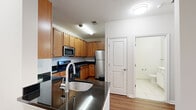 Located at 2300 Woodland Crossing Dr in Herndon, Virginia, this single-floor residence offers a thoughtfully designed layout with a clean, modern aesthetic throughout. The kitchen is a standout feature, showcasing warm honey-toned cabinetry, sleek dark granite countertops, and a full suite of stainless steel appliances including a gas range, microwave, dishwasher, and refrigerator. Wood-look flooring runs through the kitchen and living areas, adding warmth and continuity to the space. The open living area is bright and airy, benefiting from natural light that pours in through glass doors leading to a private balcony, offering views of the surrounding community. The bedrooms feature plush neutral carpeting and generous windows with exterior views, providing a quiet and comfortable retreat. The bathroom is finished with light tile flooring, a white vanity with ample counter space, a large mirror, and gold-toned hardware accents. The overall ambiance of the residence is clean, functional, and move-in ready, with a neutral color palette that complements a wide range of interior styles. Situated in the Woodland Crossing community in Herndon, VA, the residence provides convenient access to the amenities of Northern Virginia.