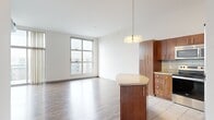 This well-appointed 3-bedroom, 3-bathroom single-floor residence offers a thoughtfully designed layout that balances comfort and functionality. The open-concept kitchen and living area serves as the heart of the home, featuring rich warm-toned cabinetry, granite countertops, a subway tile backsplash, and a full suite of stainless steel appliances including a refrigerator, range, microwave, and dishwasher. A kitchen island with a granite top provides additional prep and dining space, complemented by a stylish pendant light above. The living area extends naturally from the kitchen, finished with smooth hardwood-style flooring and a large window that invites natural light and urban views. The primary bedroom is a generously sized retreat with tall windows, hardwood-style floors, and access to a dedicated walk-in closet outfitted with wire shelving for organized storage. The additional bedrooms are carpeted and bright, offering comfortable, flexible spaces. Each of the three bathrooms is finished cleanly in neutral tones, with wood-finish vanities, granite countertops, and combination tub-shower units with accessibility grab bars. A dedicated in-unit laundry room houses a full-size washer and dryer with overhead shelving, adding everyday convenience. Throughout, the space maintains a clean, modern aesthetic with white walls and consistent finishes.